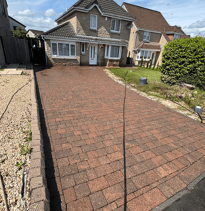 narrow red/maroon driveway of a cream/brown detached property after being power washed
