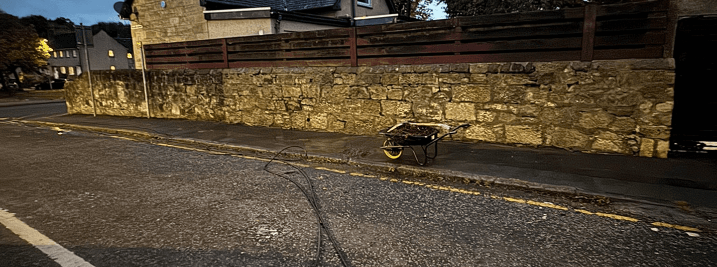 A full wheelbarrow in the middle of resident side street with power washing wires ready to go to work cleaning the driveway pavement and road.