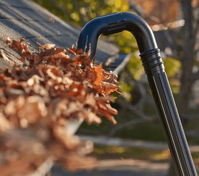 Stock Image of gutter being cleaned with a modern machine whereby the user stands at the base of the property and this machine extends in a loop to clean the gutters - leaves are in this image